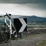 A racing bike leaning against a stone wall at the edge of a road out in the countryside.