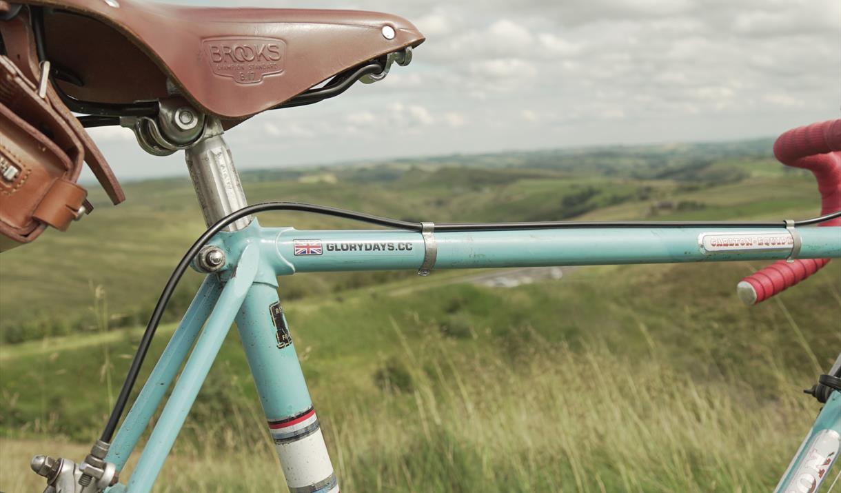 Close up of leather bike seat and bike frame, with countryside in the distance.