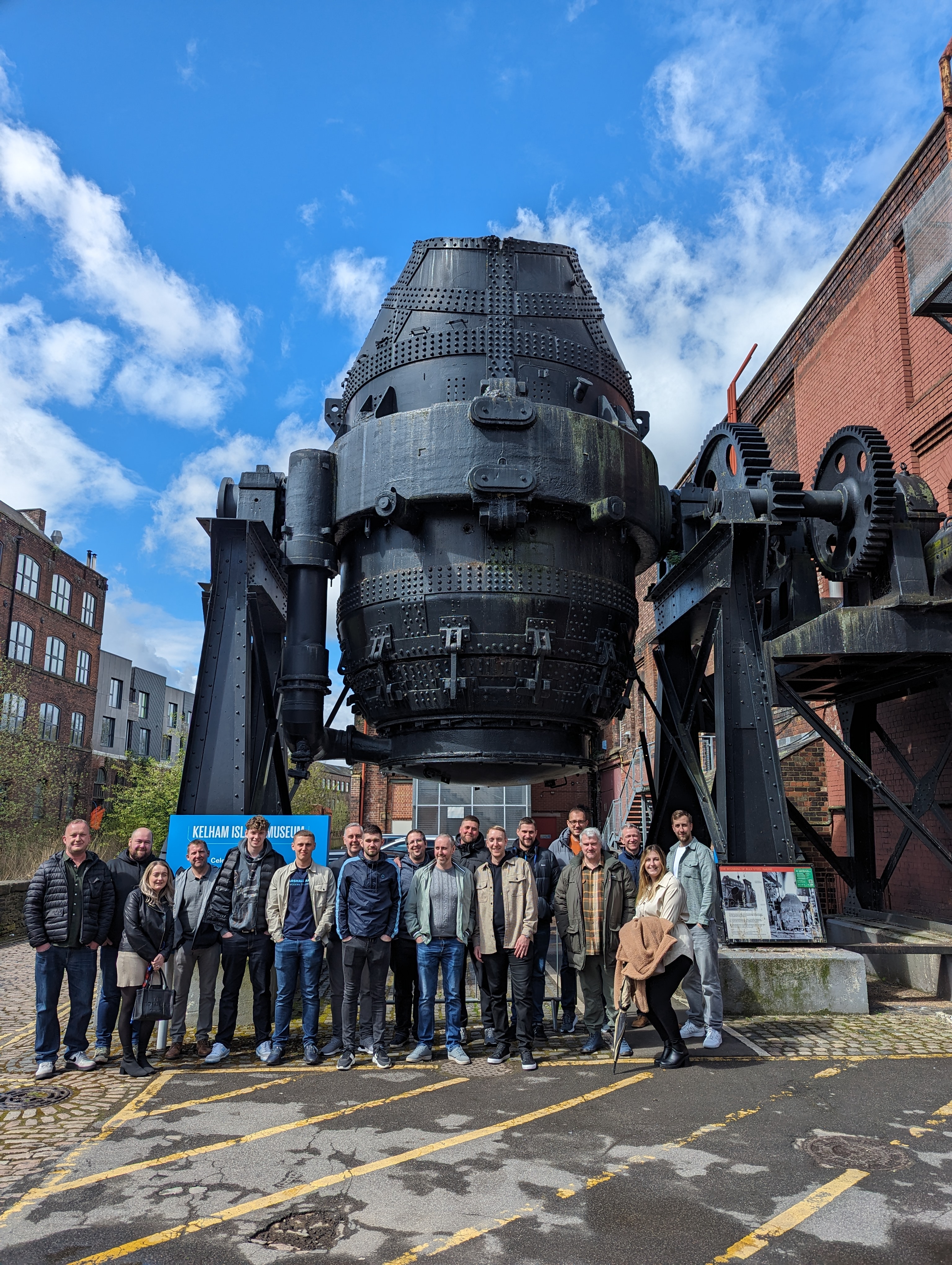 A group of people standing under the Bessemer Converter at Kelham Island. 