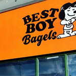 The Best Boy Bagels shop sign which features a bright orange background with the 'Best Boy Bagels' in a friendly typeface next to a cartoon of a beagle standing up and wearing a t-shirt and a baseball cap.