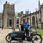 A woman and a man stand on the forecourt outside Sheffield Cathedral with a Sheffield Cycle Tours bike.