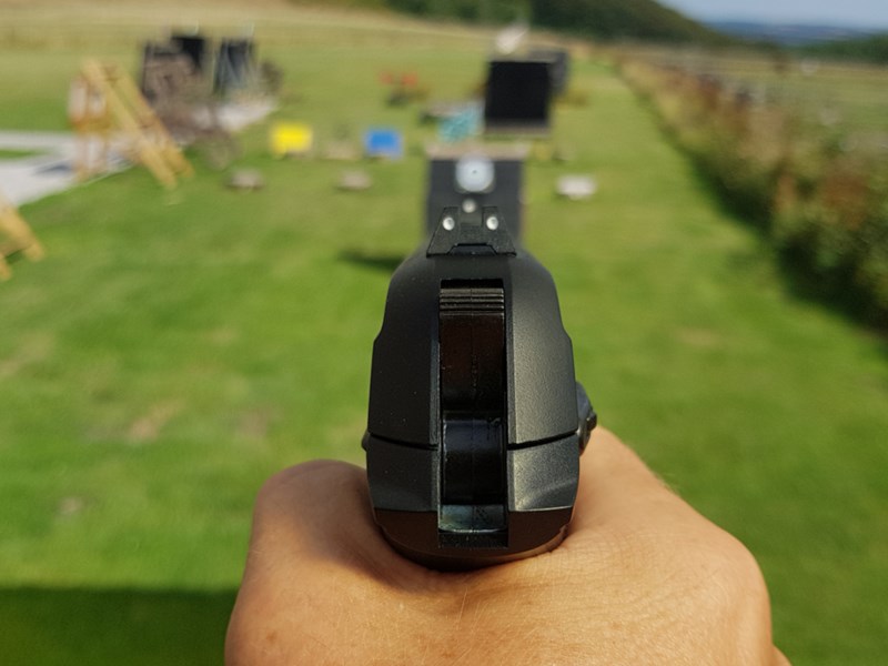 A hand holding a pistol that is aimed at a target on a shooting range.