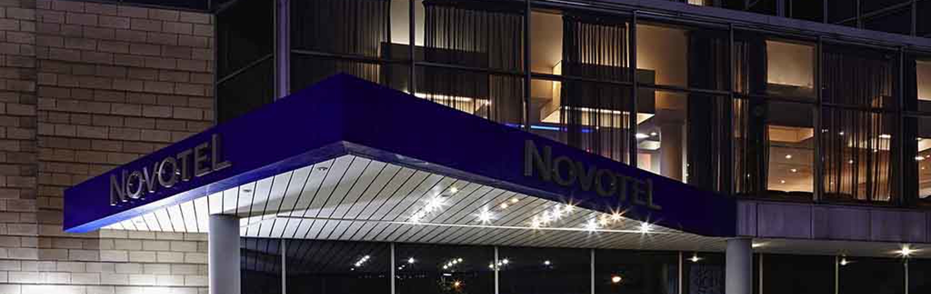 Exterior view of the Novotel hotel at night with its entrance brightly lit.