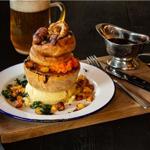 A Pieminister pie, on a table, alongside a gravy boat and a glass of beer.
