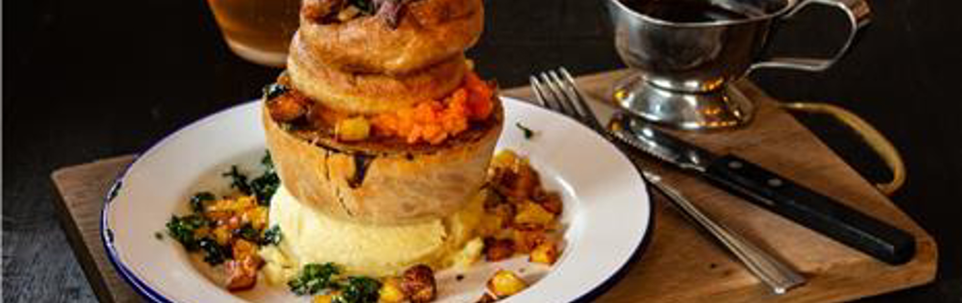 A Pieminister pie, on a table, alongside a gravy boat and a glass of beer.