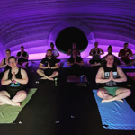 Twelve people are sat on mats on the floor doing yoga.
