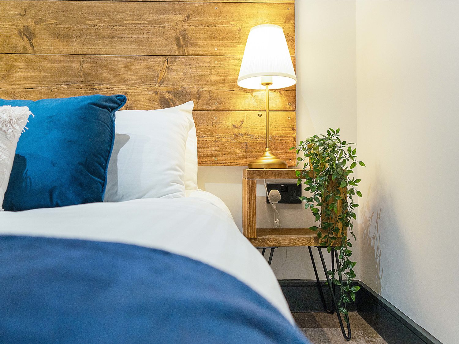 Side view of bed with a bedside table and a lit lamp.