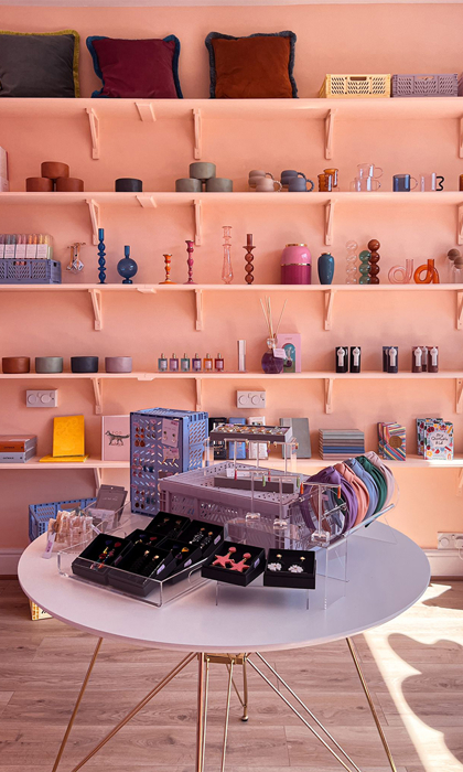 Interior shot of The Stylists Lifestyle Store with a table and shelving displaying various house wares.
