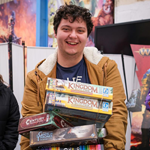 A man, laughing, is carrying a huge pile of boardgames at a previous Charity Game Swap.