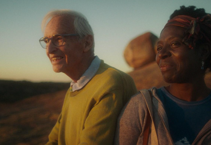 Two people sit smiling, outdoors.