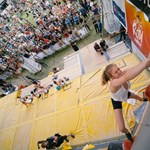 A female competitor scales a climbing wall set up on a stage on Devonshire Green. A large crowd looks on. 