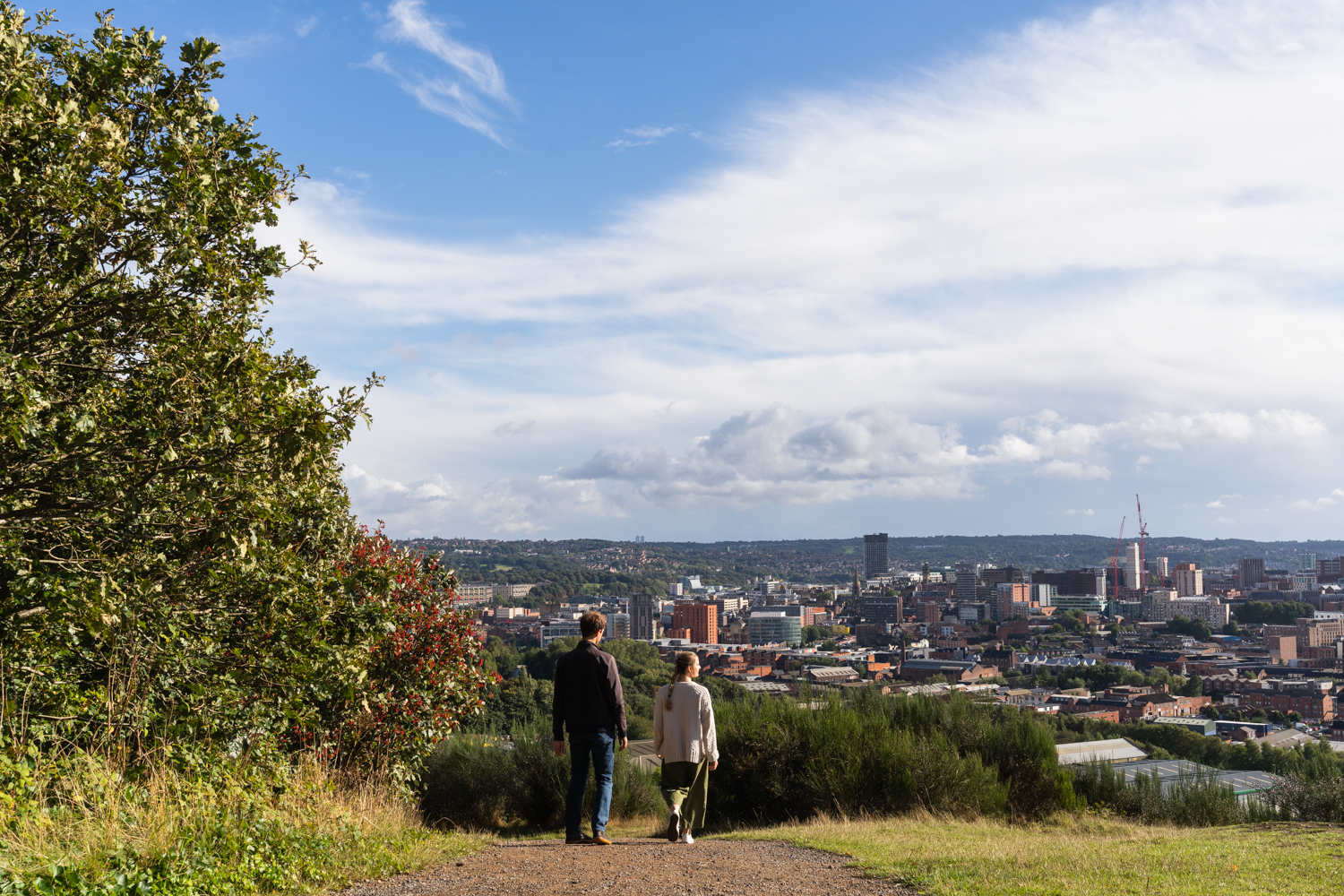 Two people walking down the hillside of Parkwood Springs with a vast view across Sheffield in front of them 