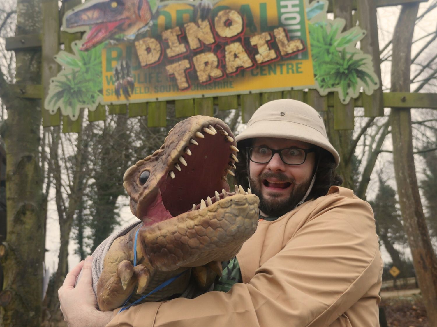 A man in a pith helmet operates a dinosaur puppet.
