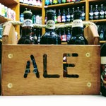 A wooden crate with the word 'Ale' cut into the side, stands on a table. It is filled with bottles of beer, and two more bottles stand on the table.