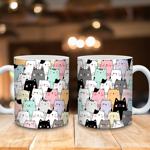 Two ceramic mugs placed on a wooden surface, each featuring a playful pattern of cartoon-style cats in pastel colors including pink, mint green, yellow, gray, and black. The background shows a softly blurred indoor setting with warm lighting.