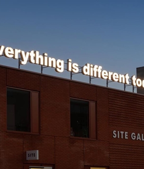 An exterior shot of the Site Gallery, in Sheffield, at dusk. On the roof is an illuminated sign reading 'everything is different today'.
