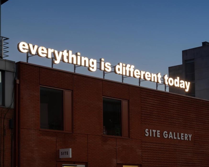 An exterior shot of the Site Gallery, in Sheffield, at dusk. On the roof is an illuminated sign reading 'everything is different today'.