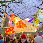 Crowds of people, holding hand-made lanterns aloft, walking in a parade. 
