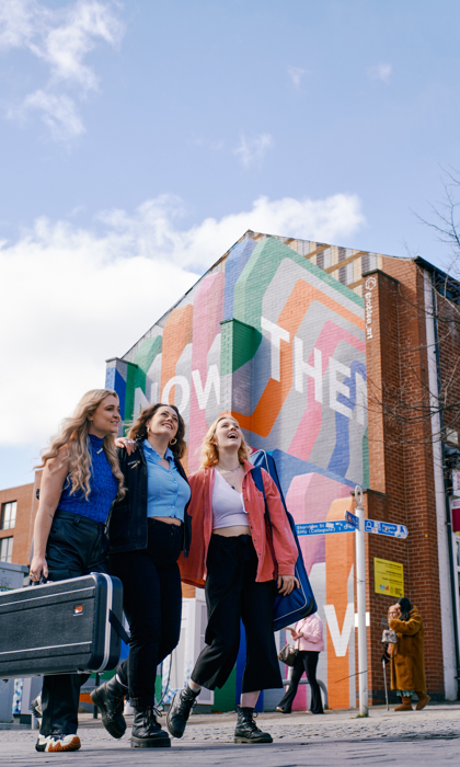 Three women stand in front of the Now Then mural on Howard Street.