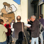 Crowd of people stood looking at 'The Snog' by Pete McKee on the side of Fagan's pub