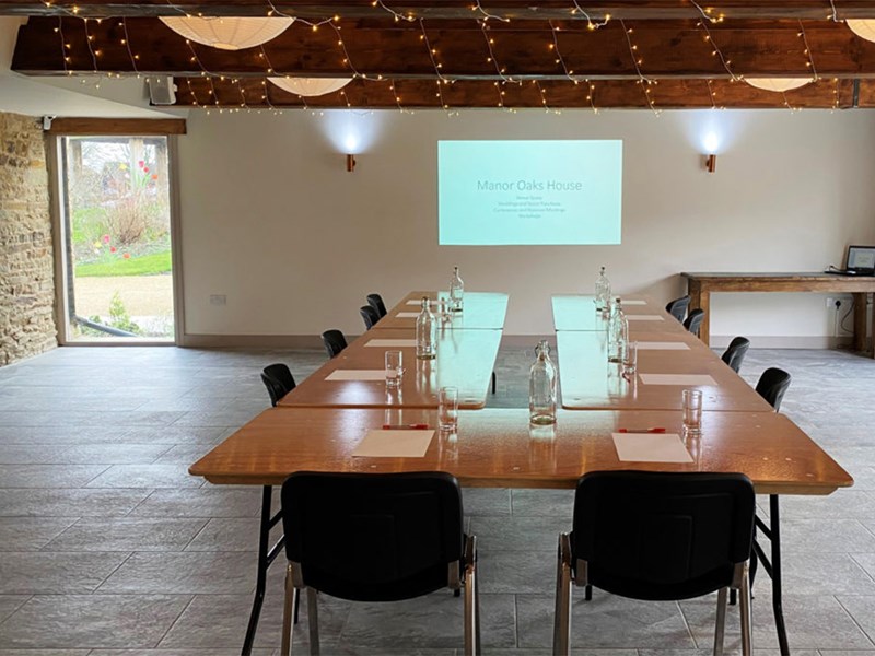 A room set up for a meeting, with a projector screen showing a slide deck, at Manor Oaks House.