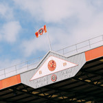 The roof of one of the stands at the Sheffield United FC stadium, with a clock and a Sheffield United FC flag flying.